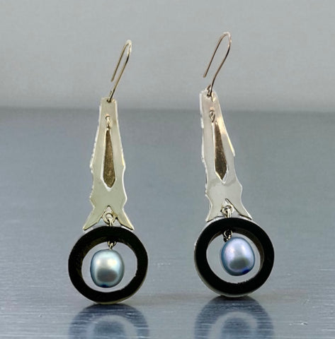 Silver earrings with black and pearl-like centers on a reflective surface